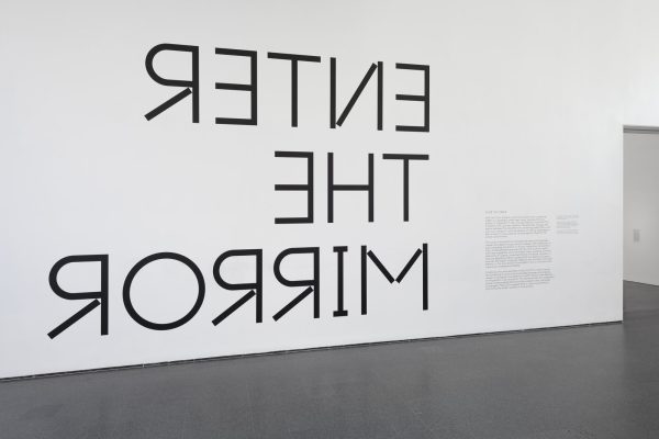 White wall with black text reading Enter the Mirror, except the text is inversed, or 