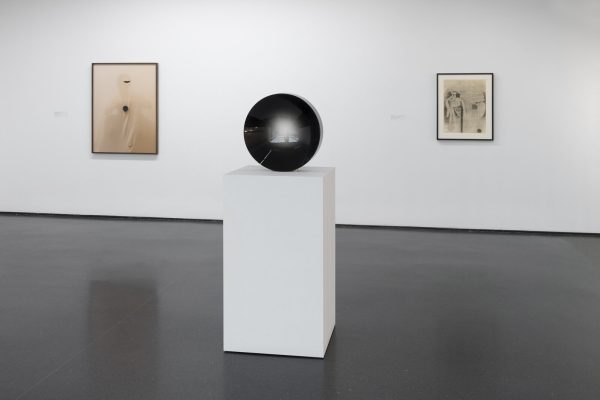 Three artworks on display in a white-walled gallery space. Two hang on the wall; one is installed on a pedestal.