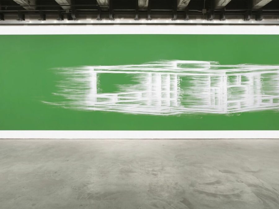 A large green artwork with a smeared white architectural design hangs on a white wall in an industrial space.