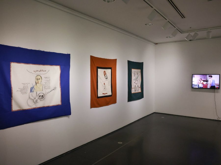 A corner of a dim gallery space with three works on the left wall; a video artwork is just visible on the right.
