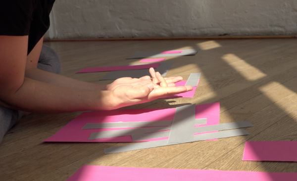 Two arms rest palms up on a floor scattered with pink paper
