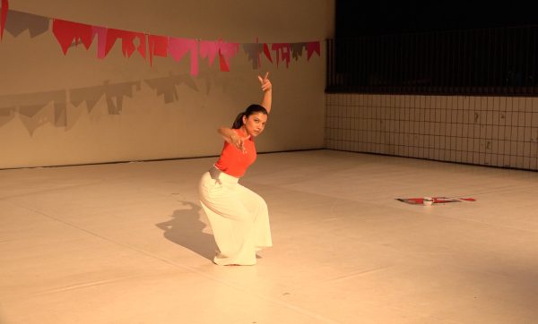 A woman poses with her left arm raised above her head in a room with red pieces of paper creating a banner above