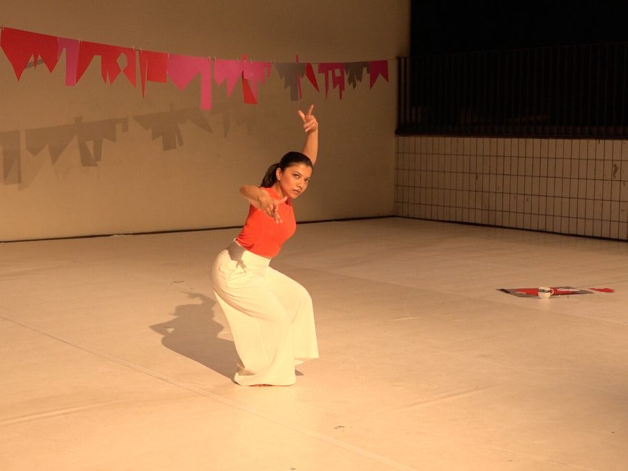 A woman poses with her left arm raised above her head in a room with red pieces of paper creating a banner above