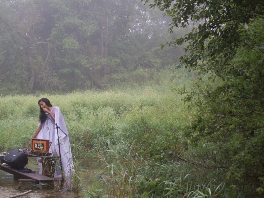 A woman performs into a microphone amid wetlands.