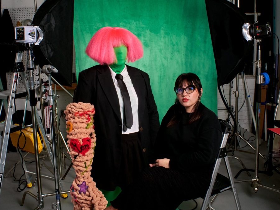 Ariella Granados sits in front of a green screen in a photography studio surrounded by props and equipment.