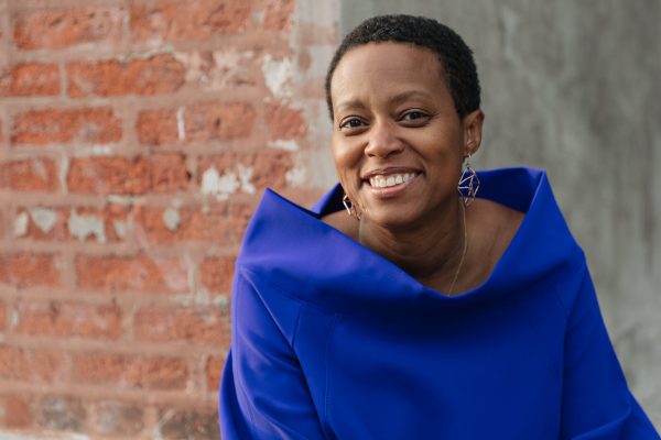 Headshot of Amanda Williams, a Black person with short black hair wearing earrings and a bright blue cowl neck sweater.