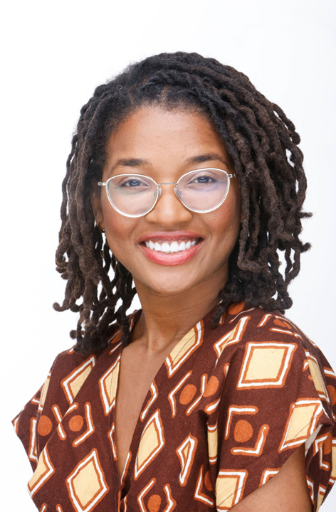 A portrait of a female-presenting person with medium-length brown hair styled in tight curls against a white backdrop