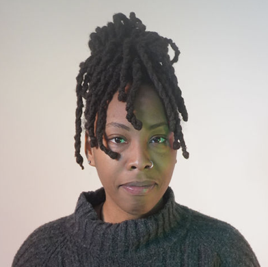 Photo of a Black person with black dreadlocks in an updo hairstyle, wearing a black turtleneck shirt.
