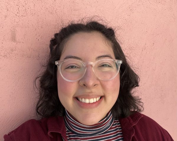 Closeup portrait of a smiling person with brown curly hair and clear glasses