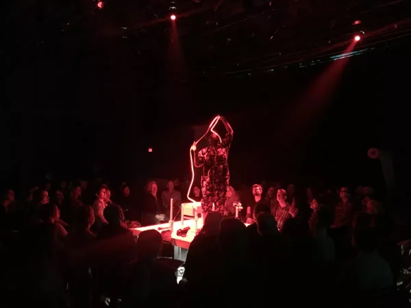 A person stands with a lit cord on a stage in the center of an audience