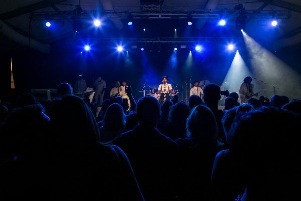A band on stage lit with blue lights playing in front of a crowd.