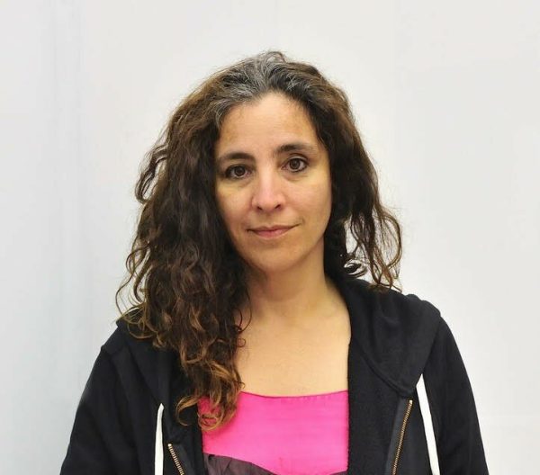 Portrait of a woman with curly brown hair standing against a white background.