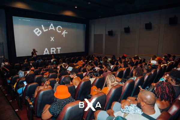 An audience in a packed theater with a screen displaying white text on a black background reading Black x Art