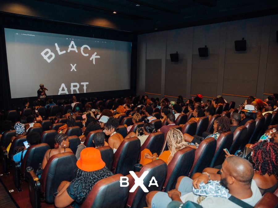 An audience in a packed theater with a screen displaying white text on a black background reading Black x Art