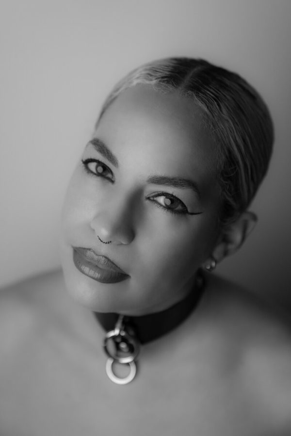 Black and white portrait of a female-presenting person with a short pixie cut, a dark choker necklace, and bare shoulders