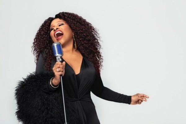 Chaka Khan dressed all in black singing into a microphone against a white background