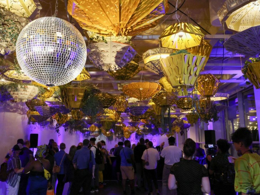 People gathered under a purple-lit room full of hanging planters and a disco ball