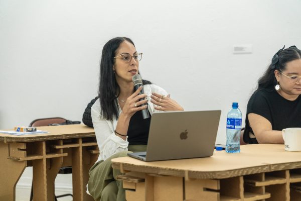 A person speaks into w microphone with a laptop open on a desk.