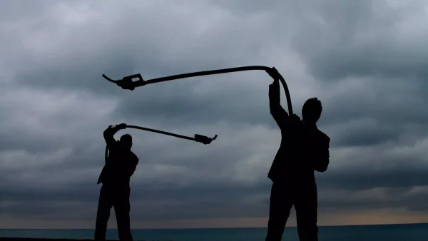 Two silhouetted figures twirl fuel hoses like lassos