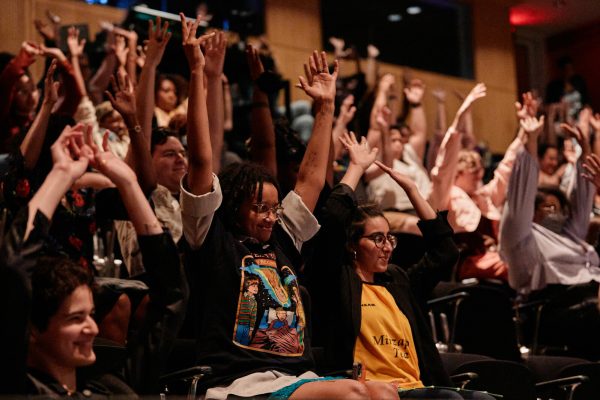 Audience members smile at the stage with their arms up in the air.