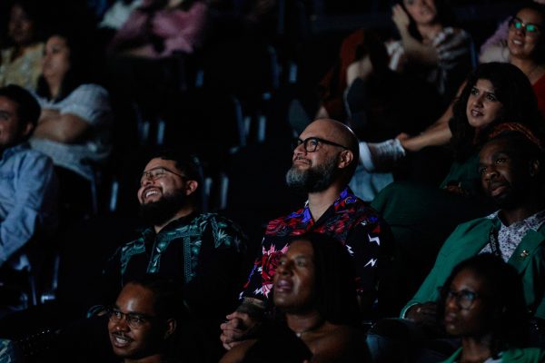 Audience members smile from stadium seating in a darkened theater