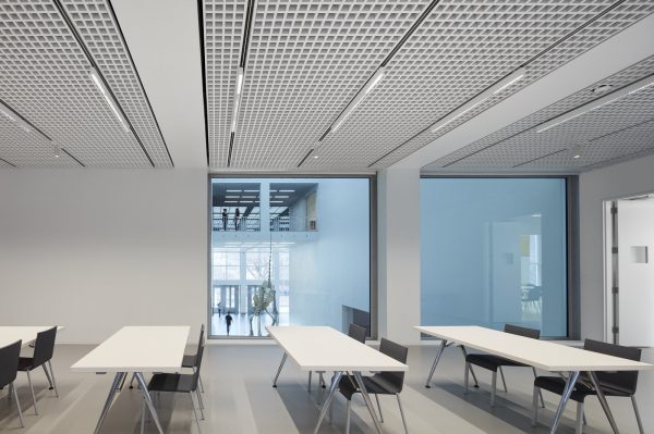 Four white tables are set in rows with two seats each in a modern venue space with square windows looking at an inner atrium space