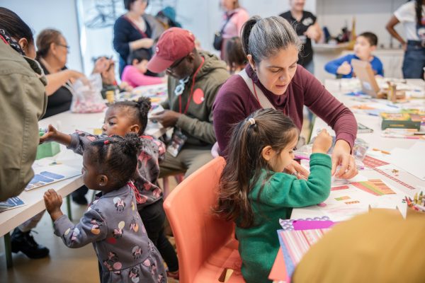 Kids and adults sit at various tables engaged in artmaking activities