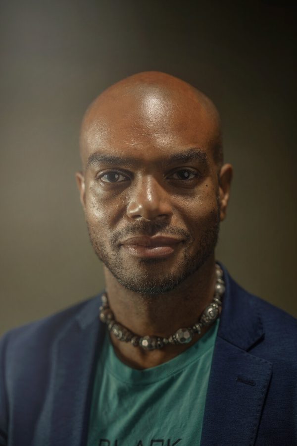 Portrait of a male-presenting person with dark skin and a bald head against a grey background