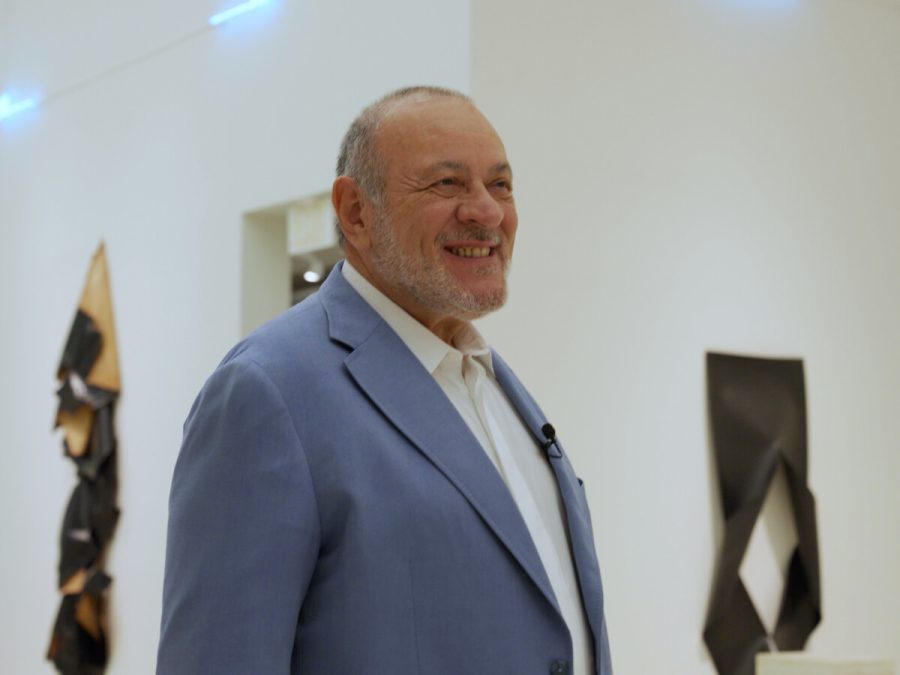 A light-skinned man in a grey suit in a gallery with art hanging on the walls behind him.