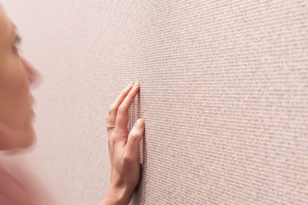 Closeup of someone using their left hand to touch a pink, patterned wall.