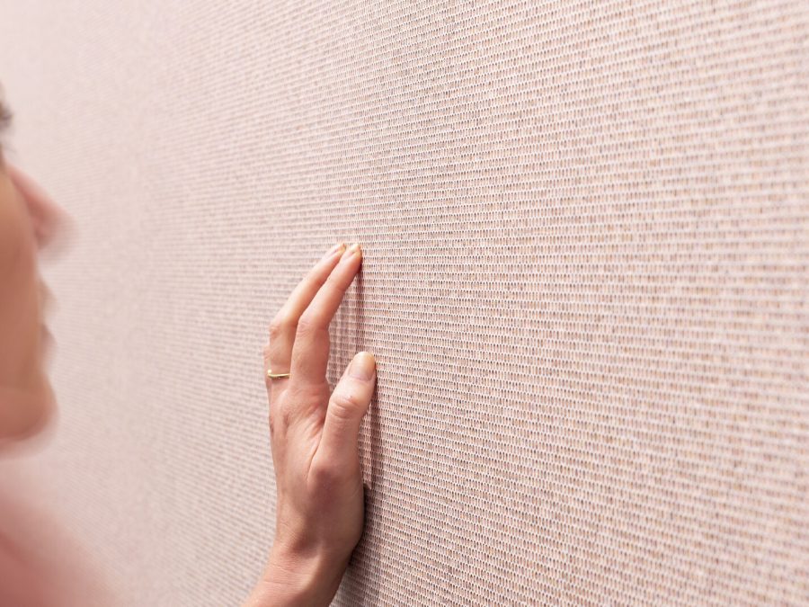 Closeup of someone using their left hand to touch a pink, patterned wall.