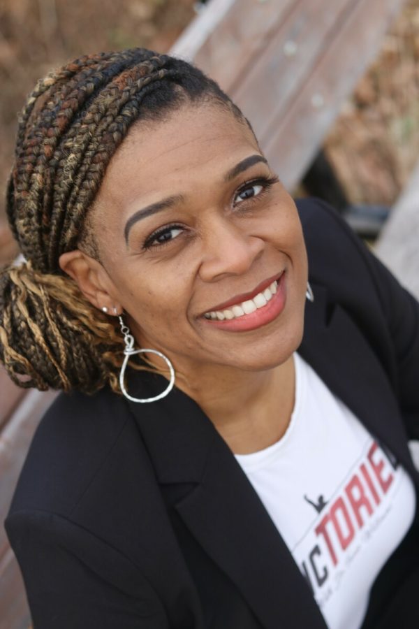 A light-skinned Black female-presenting person looking up at the camera from a park bench