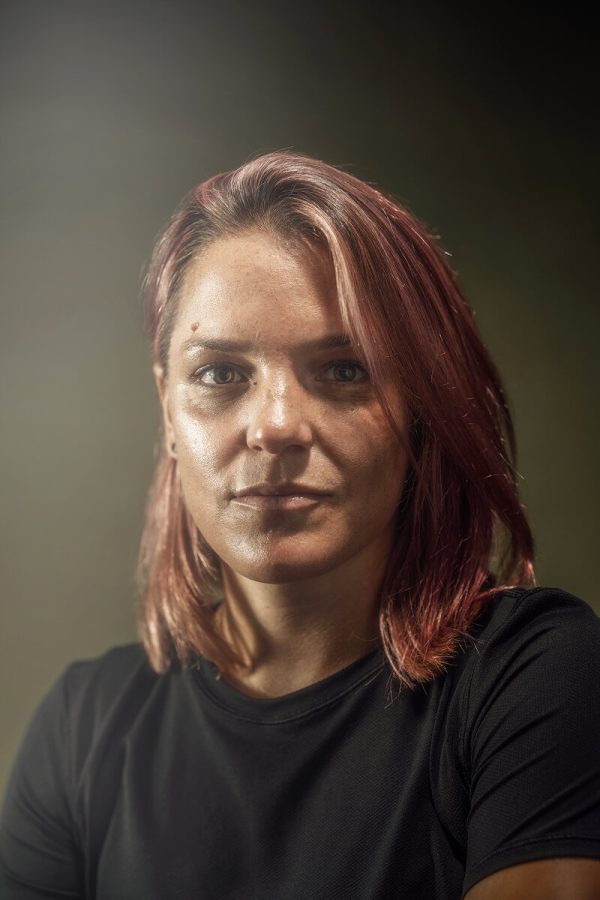Slightly hazy portrait of a woman with medium-length pink hair and an eyebrow piercing in a black shirt.