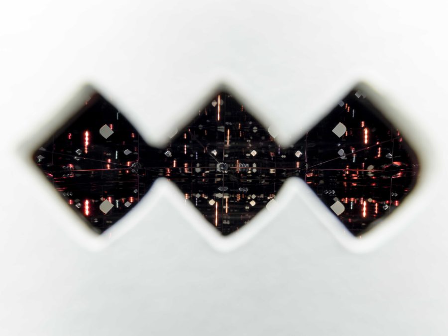Three noghtes cut out of a white wall reveal an inner room filled with light refractions.