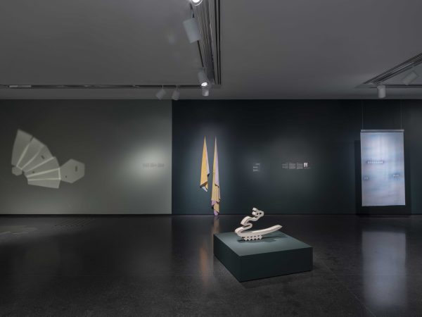 Various types of artworks hang in a dim-lit gallery space.