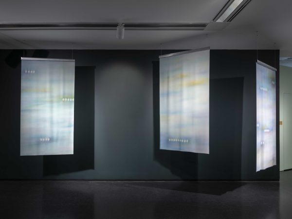 Three colorful, abstract banners hang from the ceiling in a dark teal painted room.