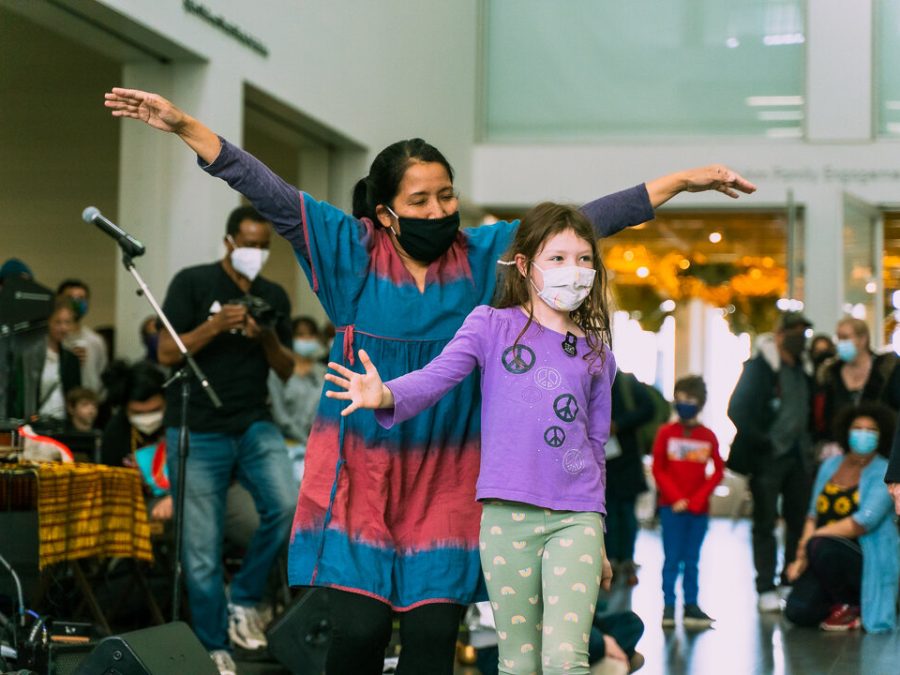 A woman and young girl dance in the MCA Commons surrounded by instruments and a crowd of people.