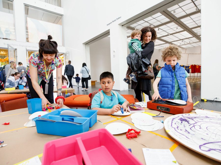 Kids and adults gather at a table filled with artmaking supplies