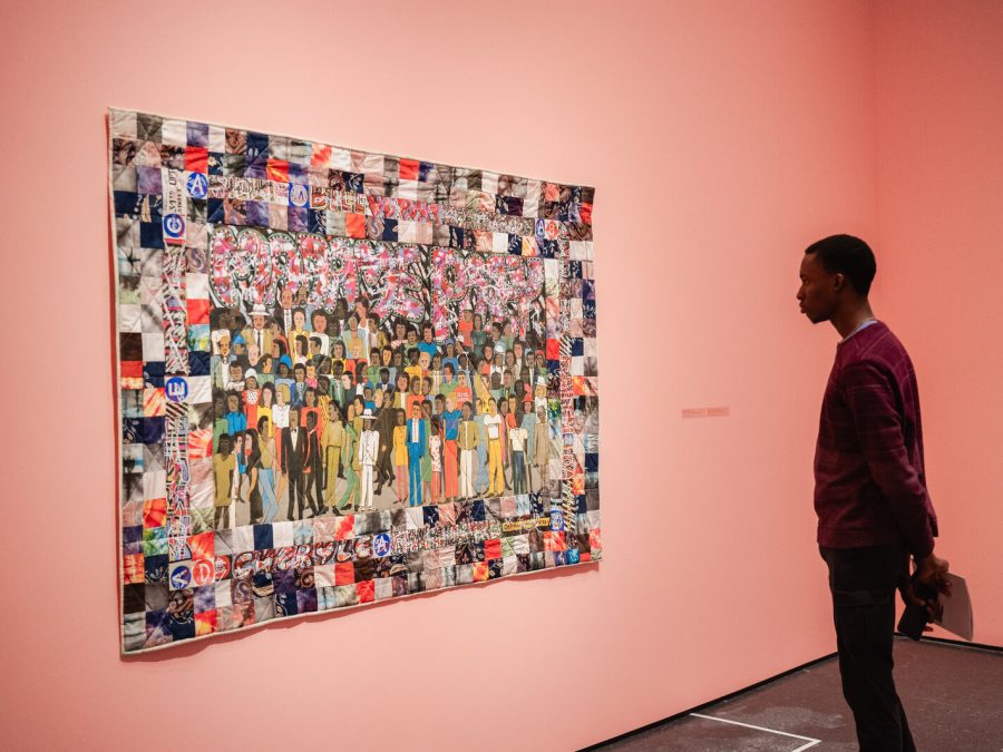 A person stands alone in a gallery painted pink, examining a work hung on the wall.