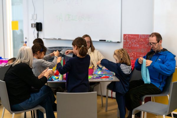 A group of children and adults sit at a table working on crafts.