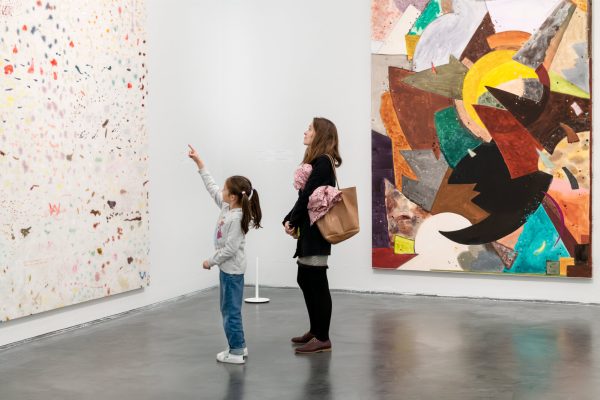 A child points at a large artwork on a wall as an adult stands nearby