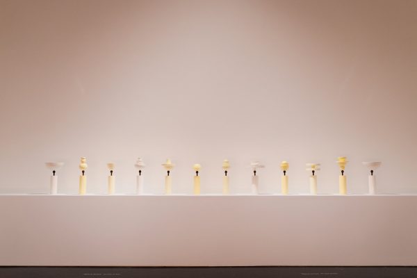 Twelve pieces of pottery of various curvaceous shapes on a platform.