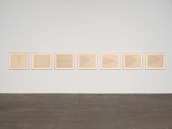 Photo of 7 framed pieces of paper with ink, hung horizontally.