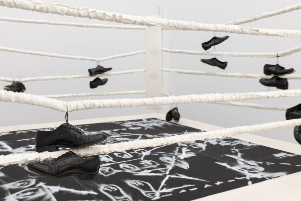 Black formal shoes hang on the ropes of a boxing ring.