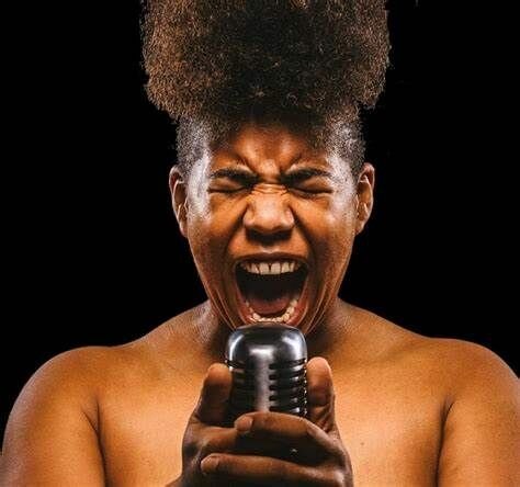 Close up portrait of a woman singing intensely into a microphone.