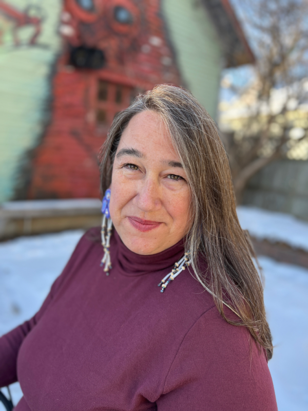 Three quarter portrait of a woman with long grey brown hair in front of an old red wall