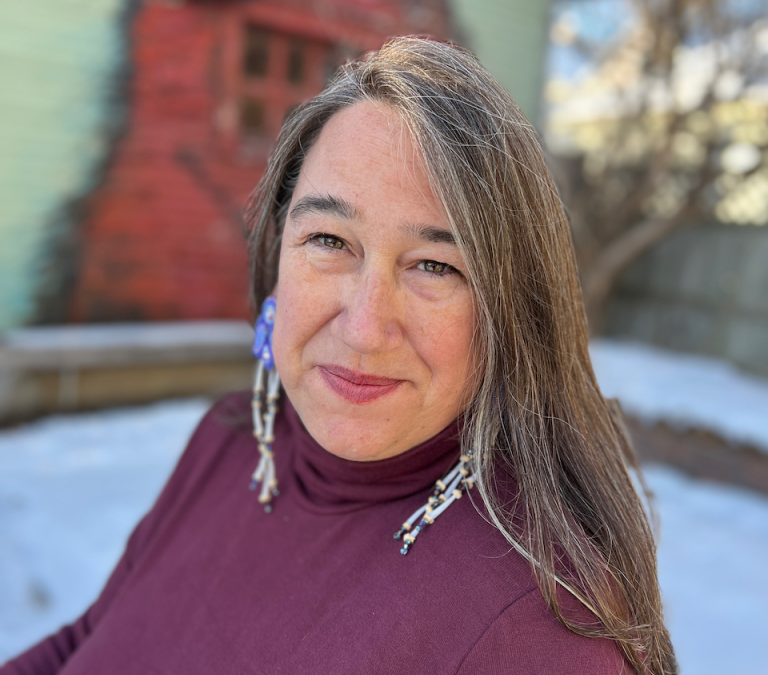 Three quarter portrait of a woman with long grey brown hair in front of an old red wall