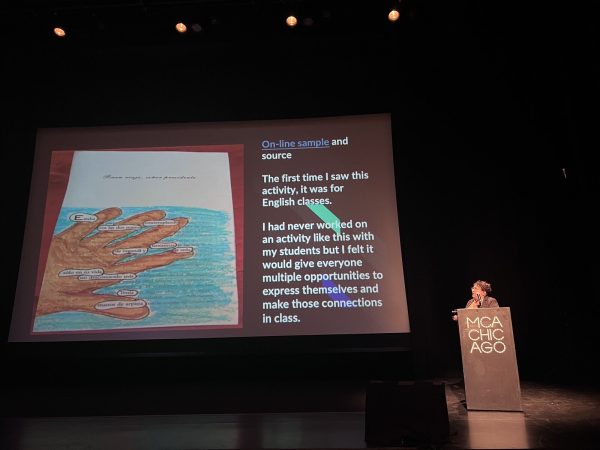 A person standing behind a podium labeled MCA Chicago looks up at a large screen projecting a presentation slide.