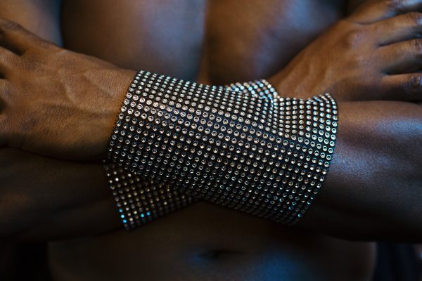 Two black arms with glittering wide wrist bands are cross against a man's chest.