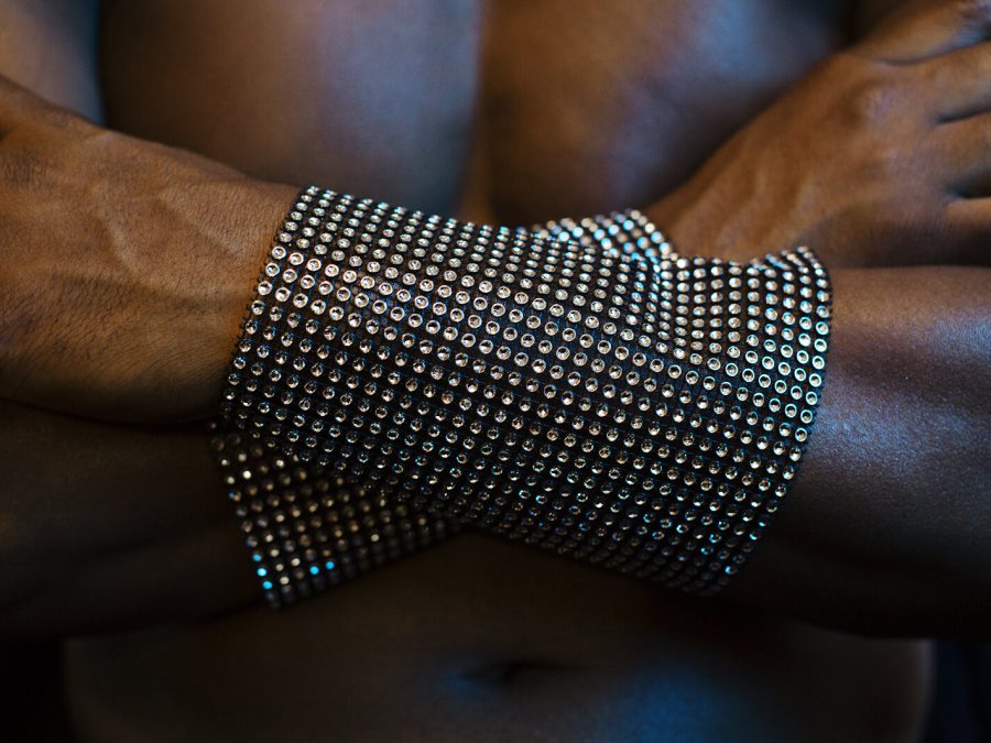 Two black arms with glittering wide wrist bands are cross against a man's chest.